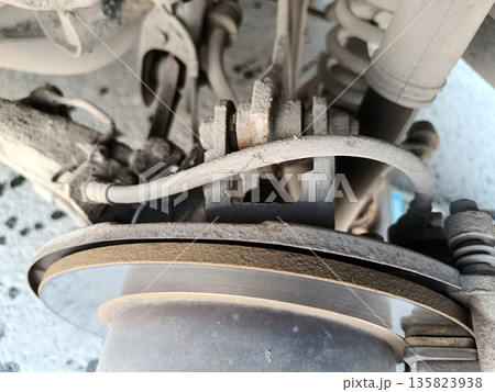 Close-up of a dusty, worn rear car brake assembly, showing the brake disc, caliper components, and brake pad material in need of inspection or service 135823938