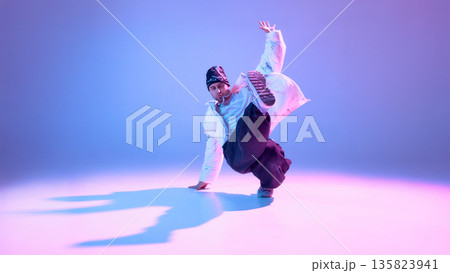 Street dancer performing high kick in studio with colorful lighting. 135823941