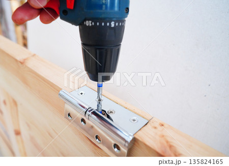Screwdriver is used to attach hinge to wooden door frame. Cordless drill  135824165
