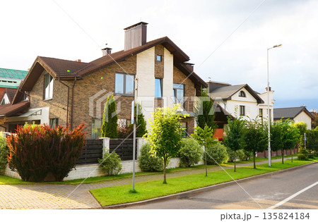 Street in residential area in suburb. Rows houses along road, sidewalk. Family house outside city.  135824184
