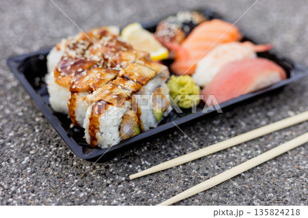 A carefully arranged sushi platter showcases various rolls topped with sauce and pieces of sashimi. The vibrant colors and textures are appealing, served with chopsticks A carefully arranged sushi platter showcases various rolls topped with sauce and pieces of sashimi. The vibrant colors and textures are appealing, served with chopsticks 135824218
