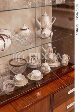 Elegant collection of vintage glassware and porcelain is carefully arranged in a wooden cabinet. Each piece reflects fine craftsmanship and timeless beauty. A perfect display for enthusiasts Elegant collection of vintage glassware and porcelain is carefully arranged in a wooden cabinet. Each piece reflects fine craftsmanship and timeless beauty. A perfect display for enthusiasts 135824220