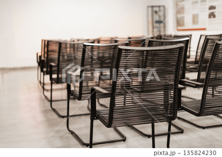 Several sleek black chairs are neatly arranged in rows within a bright gallery space. The walls feature informational displays, creating a welcoming atmosphere for visitors 135824230