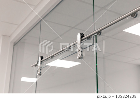 A sleek sliding glass door system showcases chrome hardware in a contemporary office. The well-lit environment highlights the clean lines and minimalistic design of the space A sleek sliding glass door system showcases chrome hardware in a contemporary office. The well-lit environment highlights the clean lines and minimalistic design of the space 135824239