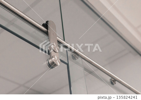 A close view of sliding glass door hardware, featuring polished metal components and a clear glass panel, set against a bright indoor background. This design emphasizes simplicity 135824241