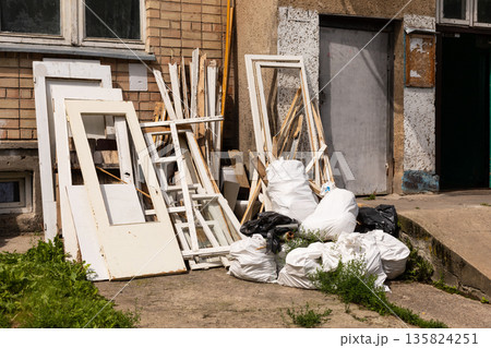 Piles of white doors, wooden frames, and garbage bags are stacked outside a building, illustrating urban waste and construction debris in a city setting during the day 135824251