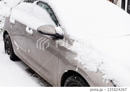 A parked car is covered with thick snow in a residential area. Snow falls steadily, creating a winter scene with no visible people around A parked car is covered with thick snow in a residential area. Snow falls steadily, creating a winter scene with no visible people around 135824267
