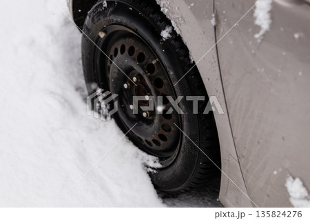 A car is unable to move due to the tire being trapped in a thick layer of snow. The scene shows snow covering the ground around the vehicle A car is unable to move due to the tire being trapped in a thick layer of snow. The scene shows snow covering the ground around the vehicle 135824276