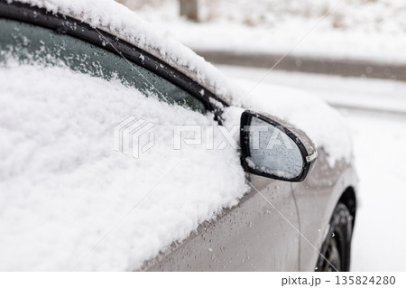 A car is parked on a road. Snow is piled on top of the car and along the windows. It is winter and flakes are falling from the gray sky. Visibility is low due to the snowfall A car is parked on a road. Snow is piled on top of the car and along the windows. It is winter and flakes are falling from the gray sky. Visibility is low due to the snowfall 135824280