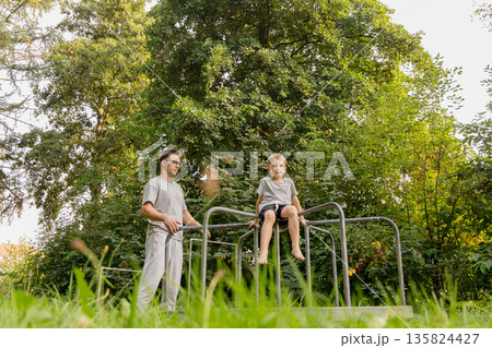 On a sunny afternoon, a father and his child share joyful moments together at a playground, engaging in fun activities among lush greenery and trees On a sunny afternoon, a father and his child share joyful moments together at a playground, engaging in fun activities among lush greenery and trees 135824427