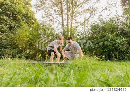 A father and his child are engaged in an enjoyable activity at a playground, surrounded by lush greenery. They are sharing laughter and curiosity, fostering a loving bond A father and his child are engaged in an enjoyable activity at a playground, surrounded by lush greenery. They are sharing laughter and curiosity, fostering a loving bond 135824432