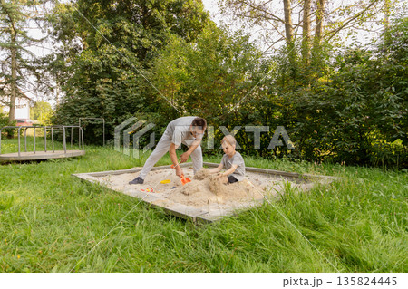 A father and his child joyfully build sandcastles in a sandbox at a playground, enjoying each other's company and the beauty of nature on a sunny day A father and his child joyfully build sandcastles in a sandbox at a playground, enjoying each other's company and the beauty of nature on a sunny day 135824445