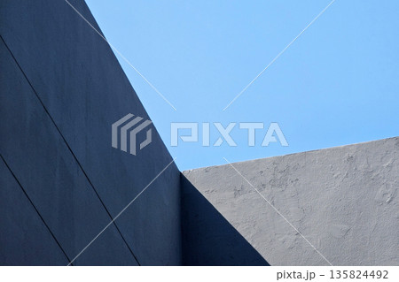 Abstract minimalist architecture of dark gray concrete wall with strong geometric lines against blue sky. 135824492