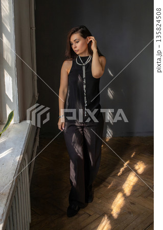 Woman in black top and dark trousers looking out window with thoughtful expression, natural light casting shadows on floor. interior designer, businesswoman, successful woman 42 years old Woman in black top and dark trousers looking out window with thoughtful expression, natural light casting shadows on floor. interior designer, businesswoman, successful woman 42 years old 135824508