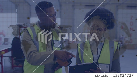 Warehouse staff wearing neon vests pointing at tablet and scanning with barcode scanner in facility 135824727