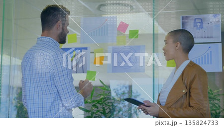 Colleagues adjusting sticky notes and using tablet at office glass wall with charts, security icon Colleagues adjusting sticky notes and using tablet at office glass wall with charts, security icon 135824733