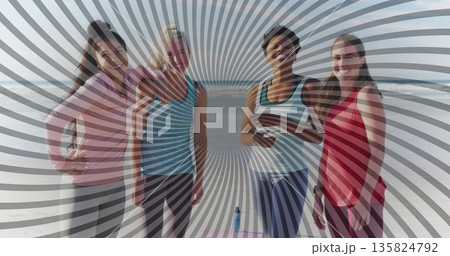 Smiling friends wearing athletic tops and leggings at oceanfront beach, with yoga mat, water bottle 135824792