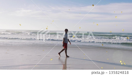 African American man walking barefoot along shoreline in red shorts, wet sand reflecting silhouette 135824818