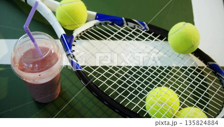 Lying blue tennis racket on ping pong table with yellow tennis balls and purple-straw smoothie cup 135824884