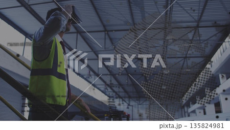 Engineer wearing safety vest using VR headset on warehouse railing, holographic overlay, copy space 135824981