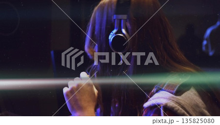 Singing recording artist wearing headphones and holding condenser mic in booth, light streaks Singing recording artist wearing headphones and holding condenser mic in booth, light streaks 135825080