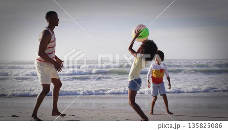 Tossing large pastel-colored beach ball between father and two children at water's edge 135825086