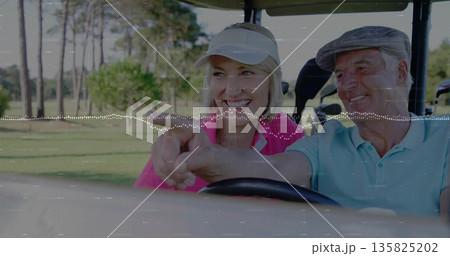 Smiling couple wearing polo shirts holding wheel pointing in golf cart on fairway, with golf clubs 135825202