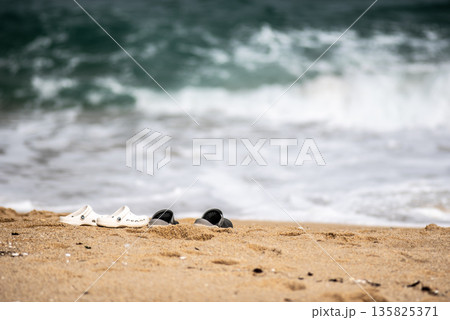 Shoes on Sandy Beach with Ocean Waves Shoes on Sandy Beach with Ocean Waves 135825371