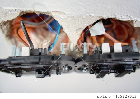 Electrical light switch with exposed wiring and mounting boxes inside white wall. Process of installing electrical sockets. Concept of electrical installation, repair, maintenance and home renovation Electrical light switch with exposed wiring and mounting boxes inside white wall. Process of installing electrical sockets. Concept of electrical installation, repair, maintenance and home renovation 135825613