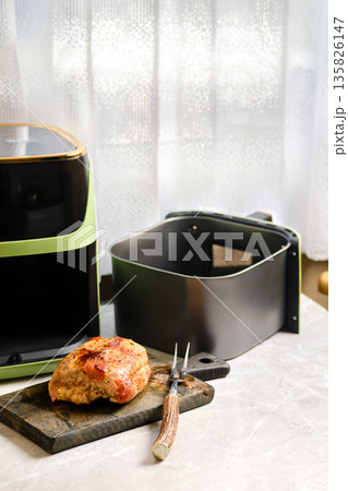 Cooked meat on cutting board beside air fryer in cozy kitchen Cooked meat on cutting board beside air fryer in cozy kitchen 135826147