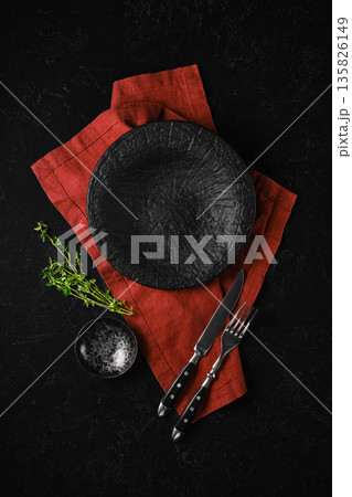 Dark plate and utensils on red cloth with fresh herbs on black background 135826149