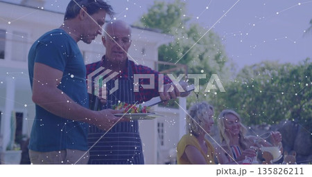Grilling senior wearing apron transferring skewers at backyard barbecue, with spatula and pitcher 135826211