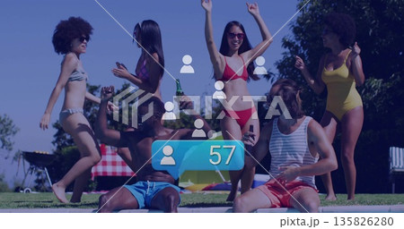 Dancing friends in swimwear splashing by backyard pool, with green bottles and picnic table 135826280