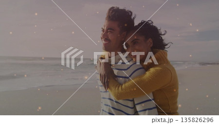 Hugging couple smiling, gazing at horizon on beach at twilight, with mustard and navy sweaters Hugging couple smiling, gazing at horizon on beach at twilight, with mustard and navy sweaters 135826296