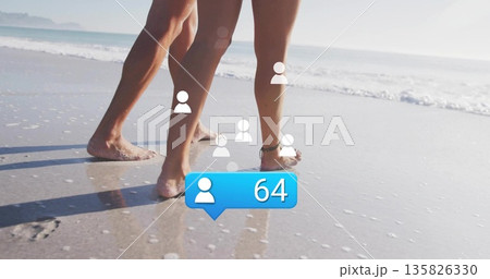 Walking couple's bare legs splashing through wet sandy shoreline, with social notification icons 135826330