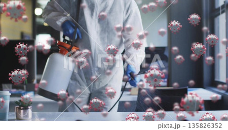 Spraying technician in coverall using sprayer on office desk with coronavirus particles, copy space 135826352