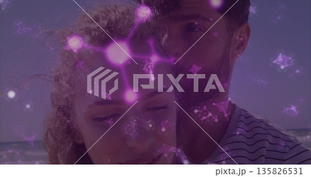 Standing couple embracing on beach, with swimsuit and striped tshirt under glowing purple patterns Standing couple embracing on beach, with swimsuit and striped tshirt under glowing purple patterns 135826531