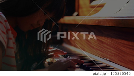 Chinese girl playing piano in home music corner, with sheet music on stand, copy space 135826546