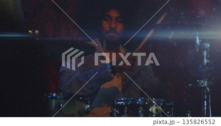 Playing drummer wearing light denim shirt over white T-shirt in dimly lit stage, with drum kit Playing drummer wearing light denim shirt over white T-shirt in dimly lit stage, with drum kit 135826552