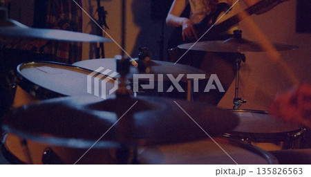 Displaying drum kit with shining cymbals in rehearsal room, with bassist playing bass guitar Displaying drum kit with shining cymbals in rehearsal room, with bassist playing bass guitar 135826563