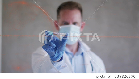 Displaying medical professional holding vaccine vial in lab, with mask, gloves and lab coat 135826570