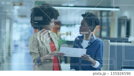 Discussing two women wearing blazer and denim shirt examining printout in office, with UI overlays 135826590