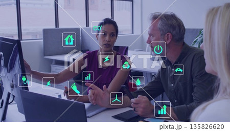 Pointing woman in sleeveless violet blouse indicating data on monitor in office, with eco icons Pointing woman in sleeveless violet blouse indicating data on monitor in office, with eco icons 135826620