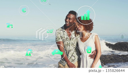 Smiling couple in patterned shirt and white dress leaning on sandy shoreline, with green eco icons 135826644