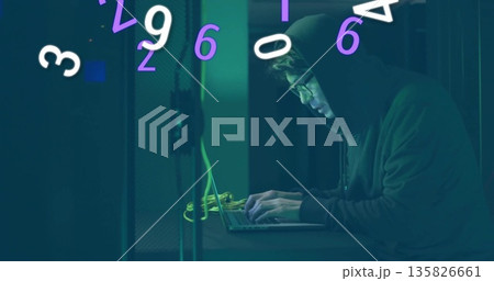 Man in hoodie typing among server racks, with laptop, yellow cables and floating digits, copy space 135826661