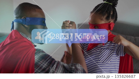 Arm wrestling father and daughter wearing masks, capes on sofa at home, with follower count overlay Arm wrestling father and daughter wearing masks, capes on sofa at home, with follower count overlay 135826687