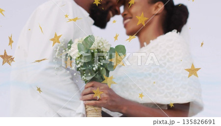 Standing couple wearing white sharing wedding moment at seaside, holding bouquet and golden stars Standing couple wearing white sharing wedding moment at seaside, holding bouquet and golden stars 135826691