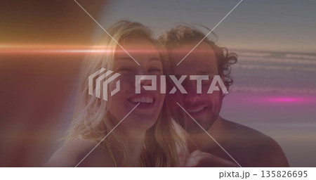 Smiling adult woman and man taking close-up selfie at beach during golden hour, with lens flare Smiling adult woman and man taking close-up selfie at beach during golden hour, with lens flare 135826695
