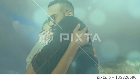 Hugging couple embracing closely outdoors under blue sky above rocky outcrop, with round eyeglasses Hugging couple embracing closely outdoors under blue sky above rocky outcrop, with round eyeglasses 135826696
