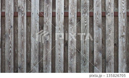 Aged gray textured wooden planks in the structure of a rustic fence, beautiful aged boards attached to a sheet of plywood with a rusty iron insert as a background texture 135826705